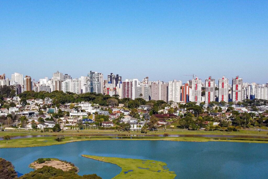 A cidade de Curitiba vista do alto. À frente, o lago do Parque Barigui. Ao fundo, uma linha de prédios