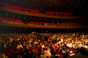 Interior do teatro Guaíra. Várias cadeiras em múltipos andares olhando da esquerda pra direita, em direção ao palco.