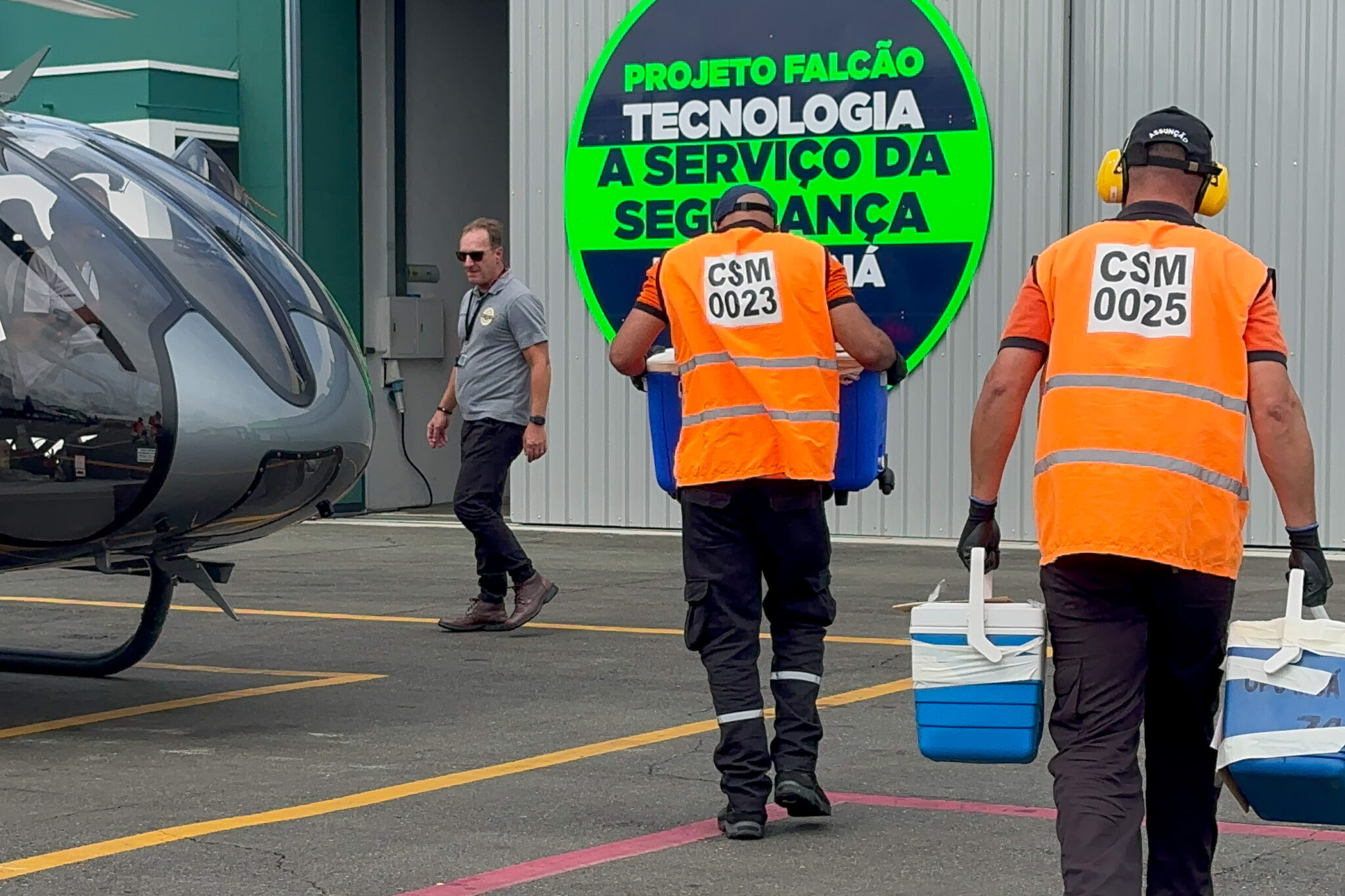 Duas pessoas com coletes refletores carregam geladeiras portáteis para fora de um helicóptero