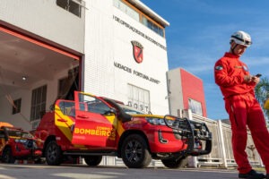 Bombeiro usa o celular em frente a quartel dos bombeiros com veículo estacionado dentro