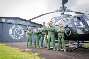 5 policiais civis posam em frente a helicóptero.