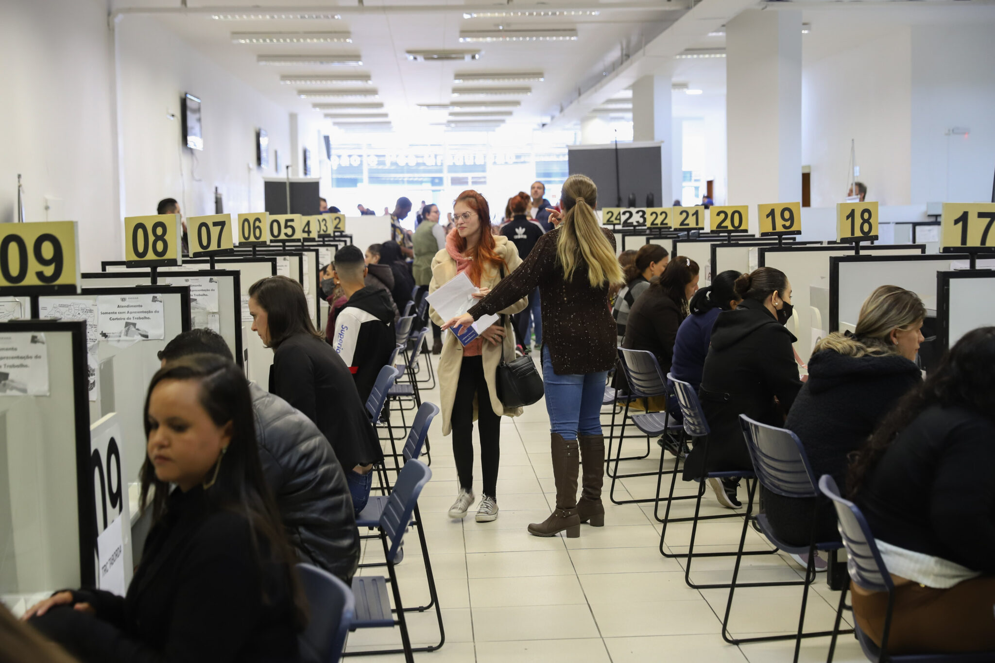 Pessoas se encaminham a vários cubículos para consultar vagas de emprego