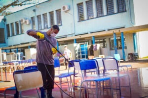 Funcionário usa maquina de água pressurizada para limpar cadeiras de escola atingida por enchente