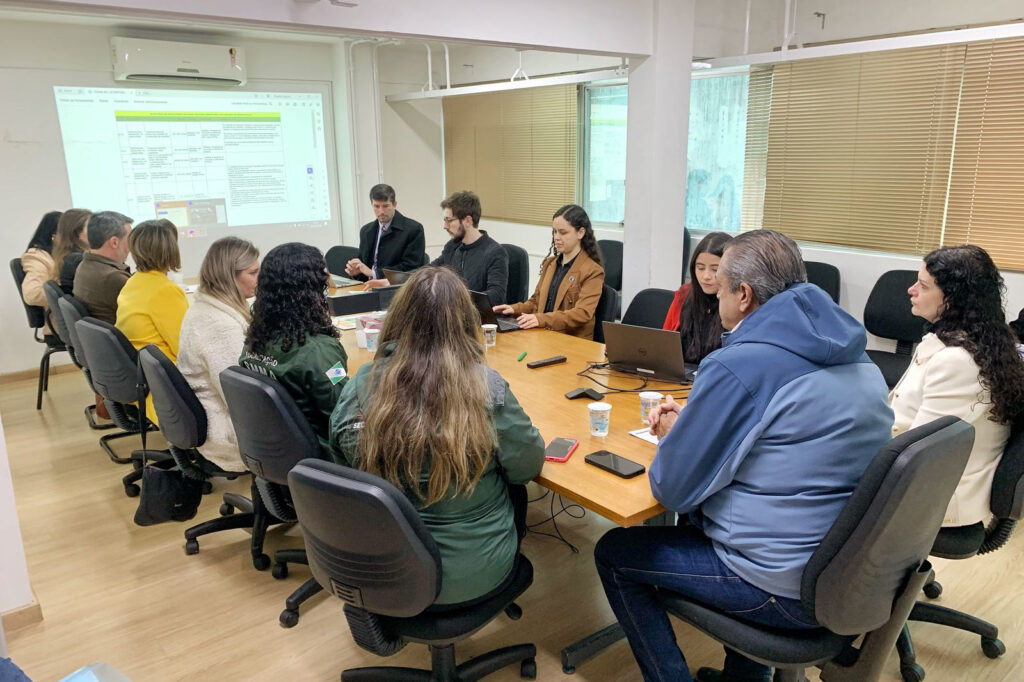 Pessoas em volta de mesa observam projeção