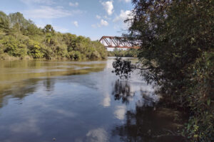 Beira de rio com ponte ao fundo.