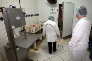 Interior de cozinha industrial com dois inspetores de jaleco.