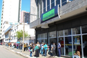 Fachada da agência do trabalhador com fila de pessoas na calçada.