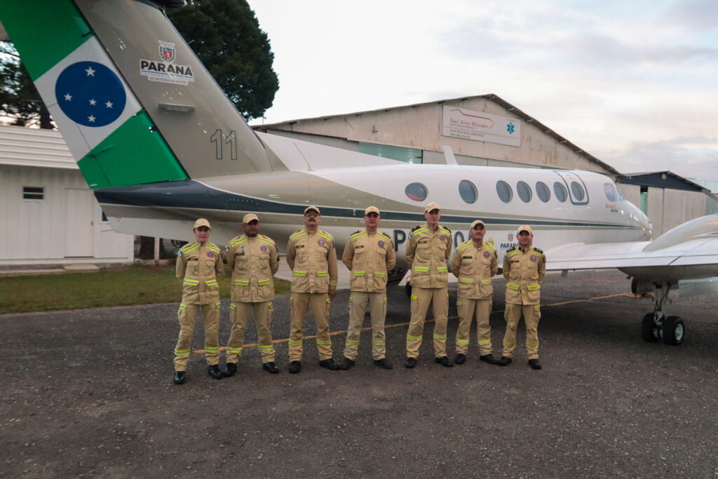 Sete membros do corpo de bombeiros posam em frente a avião.