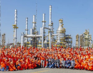 Em primeiro plano, trabalhadores e comitiva de presidente Lula posam para foto. Todos estão vestindo macacões laranjas. Ao fundo, torres de metal da fábrica de fertilizantes.