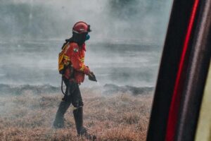 Bombeiro com equipamento de incêndio circula por grama queimada