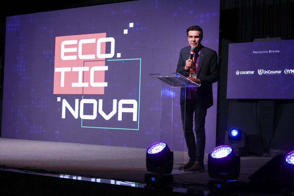 Uma pessoa num púlpito fala ao microfone. Atrás dela, numa tela está escrito "Eco Tic Nova" em letras caixa alta.