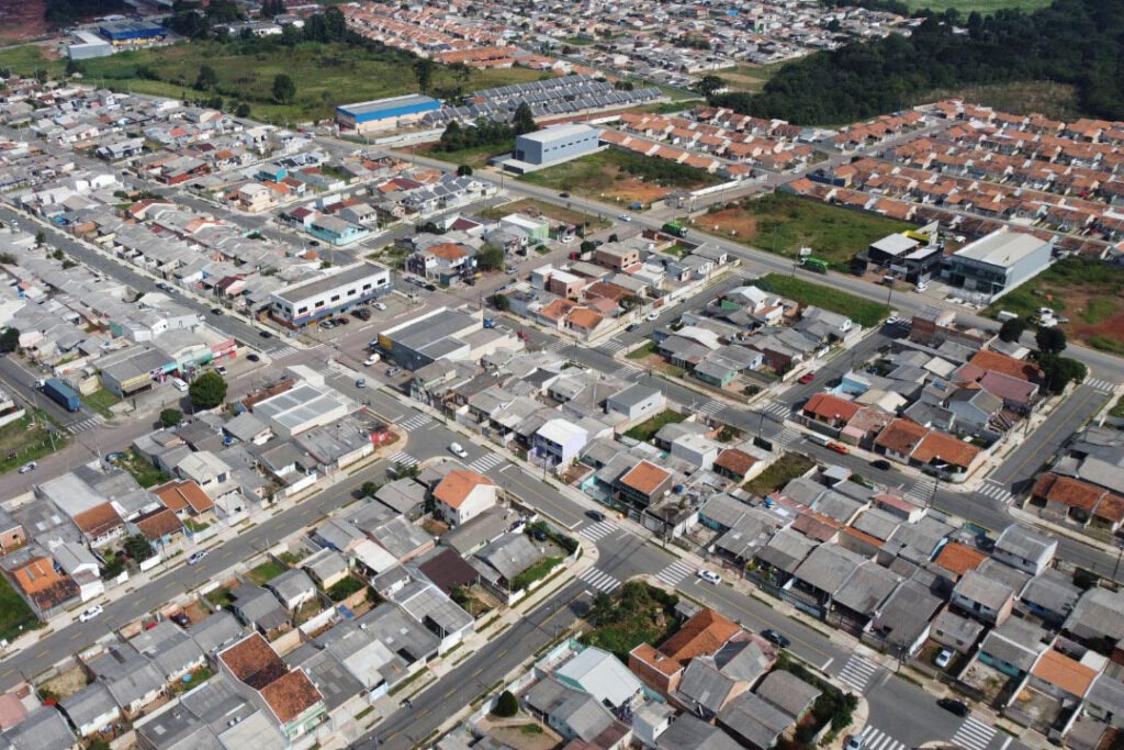 Foto aérea de bairro em Fazenda Rio Grande. Poucos prédios tem mais de um andar térreo. Boa parte das casas tem telhados cinza e algumas poucas tem telhas laranjas