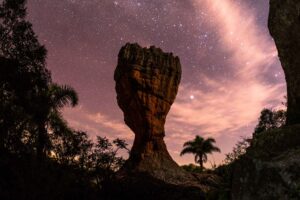 Foto noturna de formação rochosa no Parque Vila Velha. Ao fundo, o céu estrelado está bem iluminado.