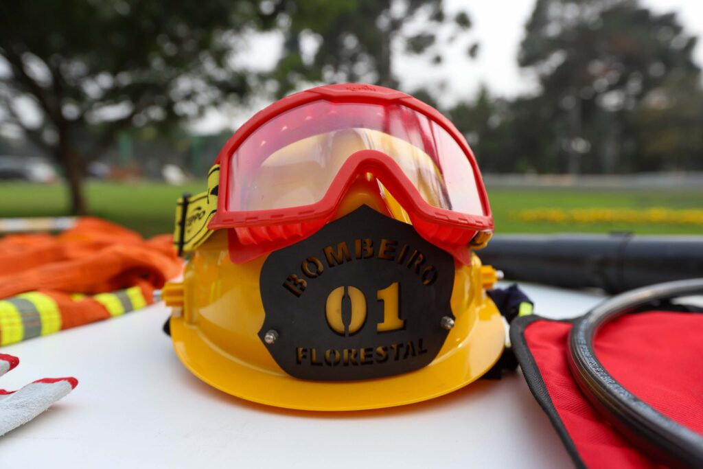 Capacete amarelo com óculos vermelho e uma placa preta escrita Bombeiro Florestal 01