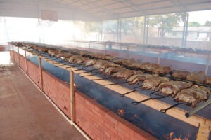 Churrasco de boi na brasa. Várias peças de carne em espetos enfileirados.