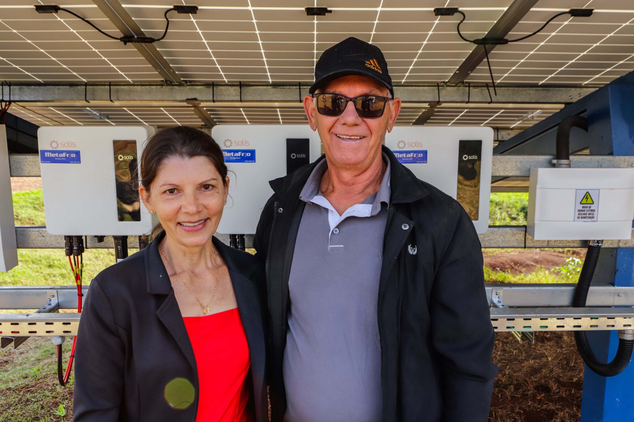 Casal posa atrás de estrutura de placas solares