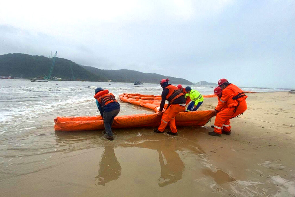 Pessoas uniformizadas arrastam barreira flutuante para a praia