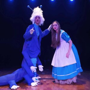 Atores em palco de teatro. Á esquerda, a lagarta e a direita, Alice.