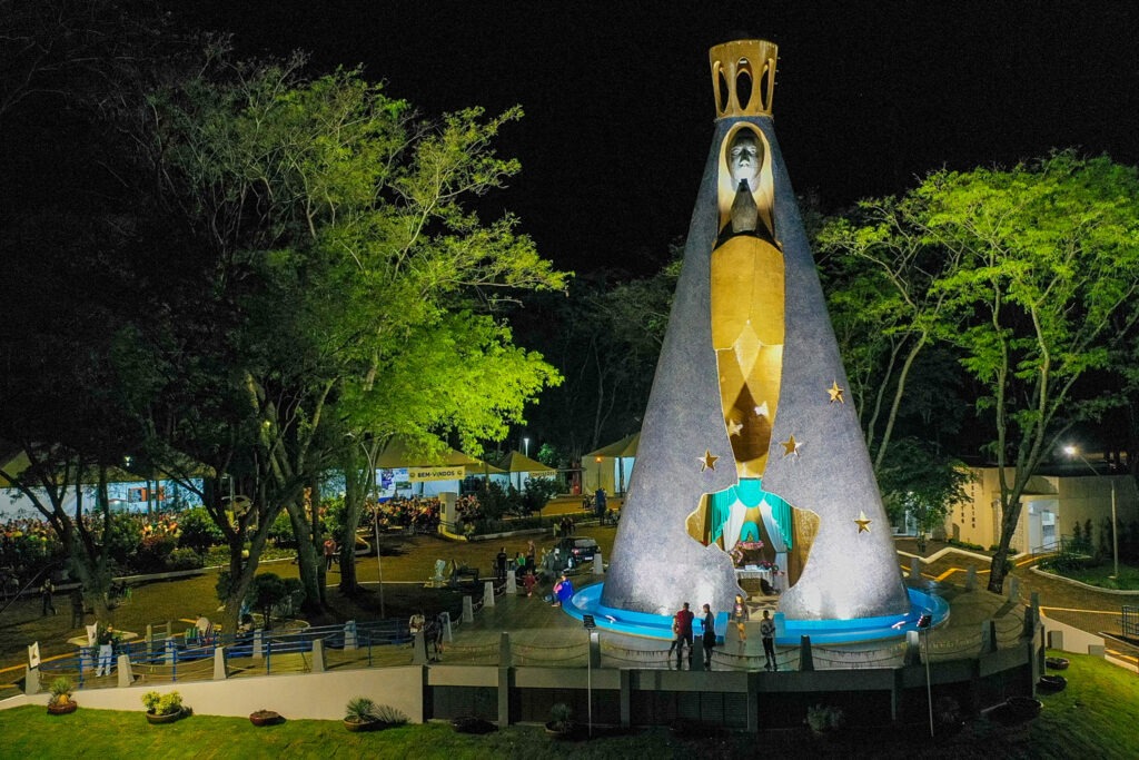 Estátua em praça a noite. O manto azul da santa imita um formato de cone.