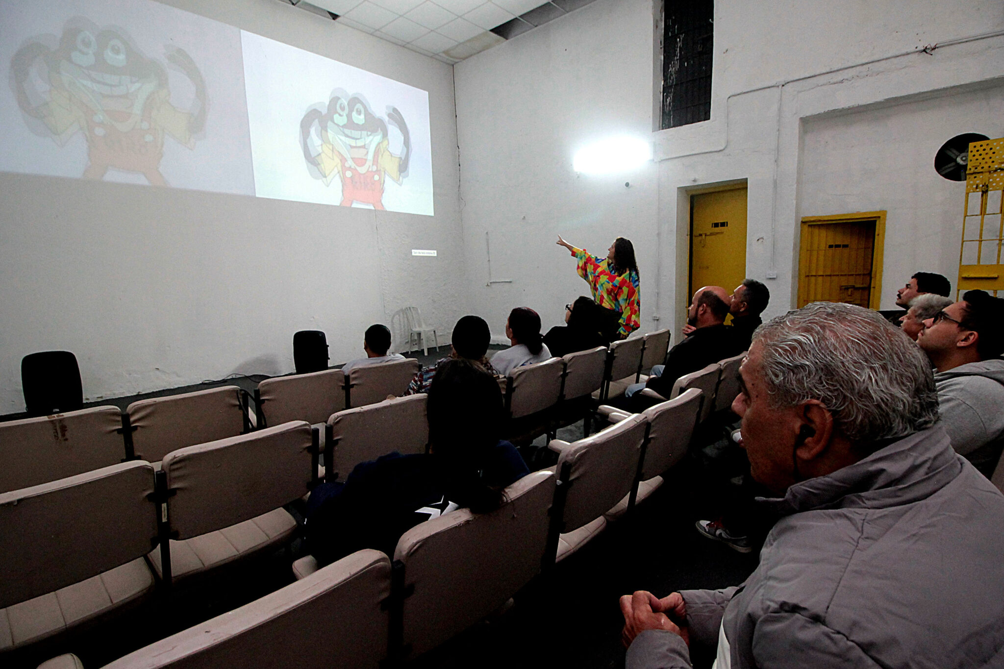 Sala de cinema improvisada. Ao fundo, uma porta reforçada de metal.