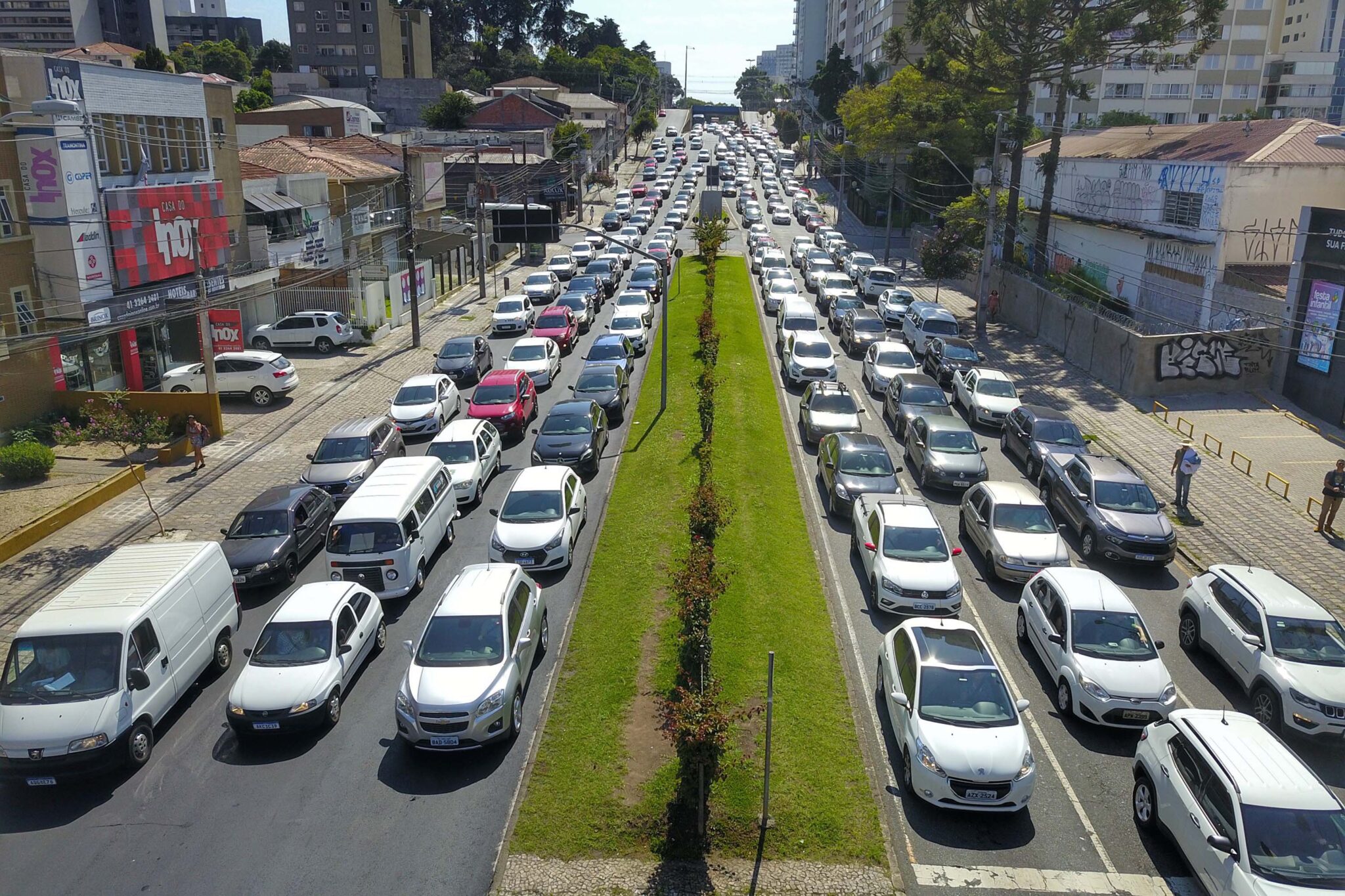 Seis pistas de carros separadas por um canteiro de grama com cerca. Todas as pistas estão completamente cheias de veículos