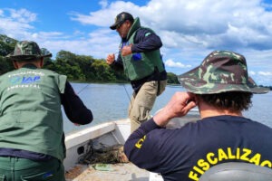 Fiscais em barco recolhem rede em rio