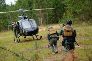 Dois policiais fortemente armados correm em direção a helicoptero em clareira