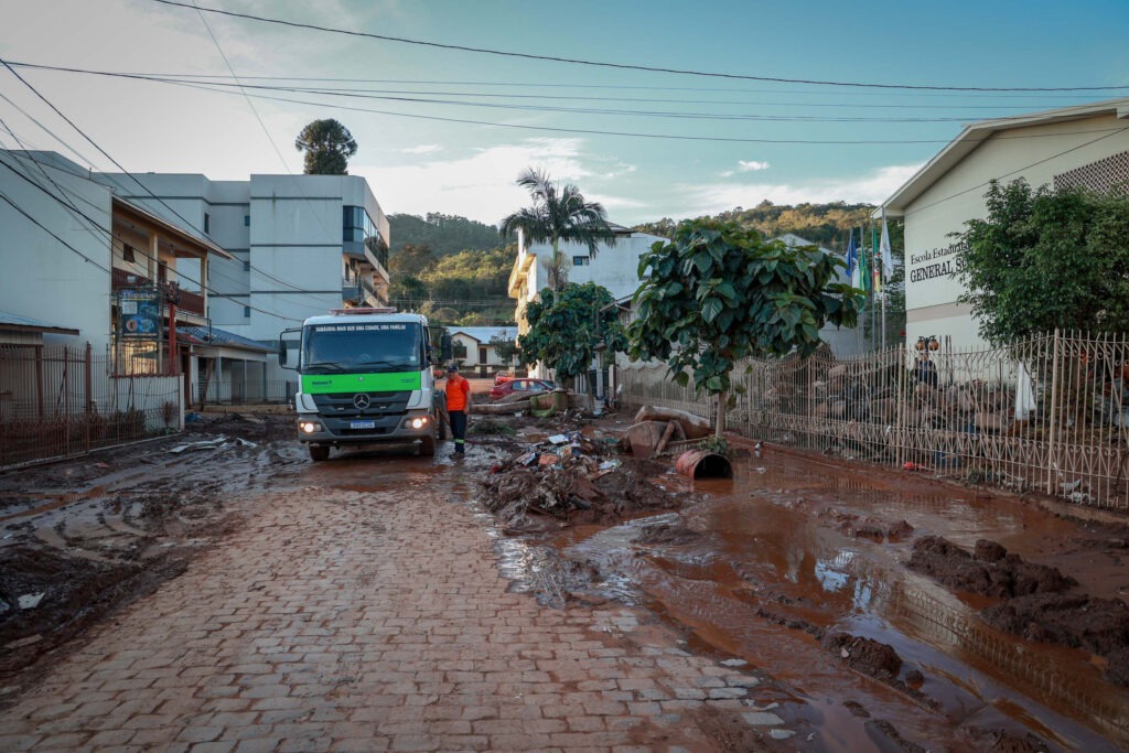 Um caminhão passa por uma rua devastada com lama nas laterais.