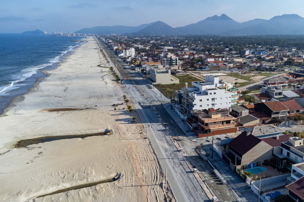 Imagem aérea de cidade litorânea com prédios baixos na beira da praia sendo separados da areia apenas por uma rua de mão dupla