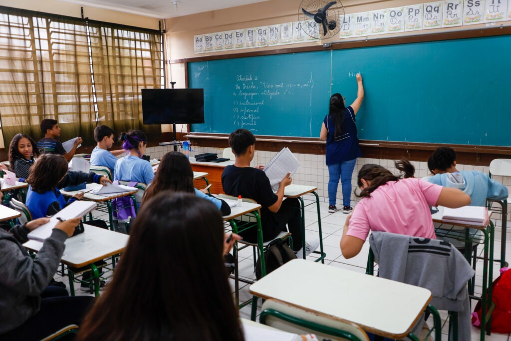 Alunos observam professora que escreve em quadro-negro