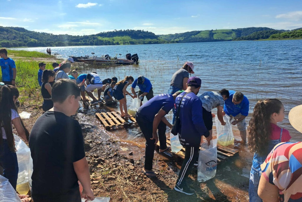 Pessoas fazem a soltura de peixes em beira do Rio Iguaçu