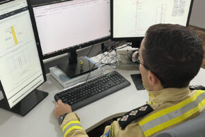 Bombeiro fardado olha para três telas de computador