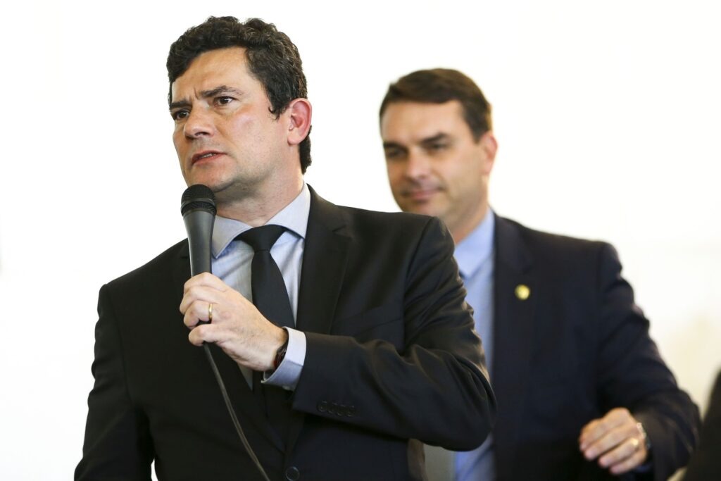 Sergio Moro em primeiro plano e Flavio Bolsonaro no segundo. O senador do PL no Rio de Janeiro convidou o paranaense para se filiar ao seu partido