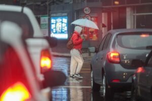 Mulher com guarda chuva enfrenta o trânsito no centro de uma cidade