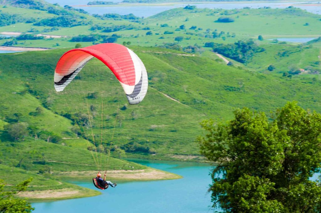 Homem faz parasailing em paisagem com represa e árvores ao fundo