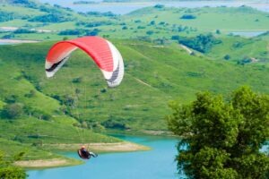 Homem faz parasailing em paisagem com represa e árvores ao fundo