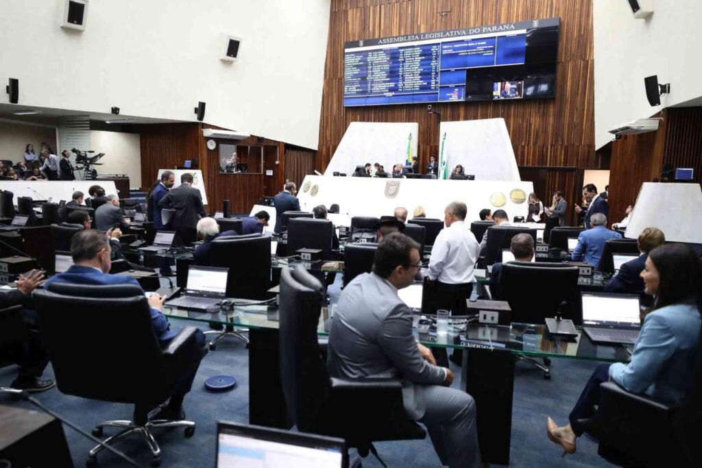 Deputados vistos lateralmente sentados em suas cadeiras durante sessão da Assembleia Legislativa do Paraná