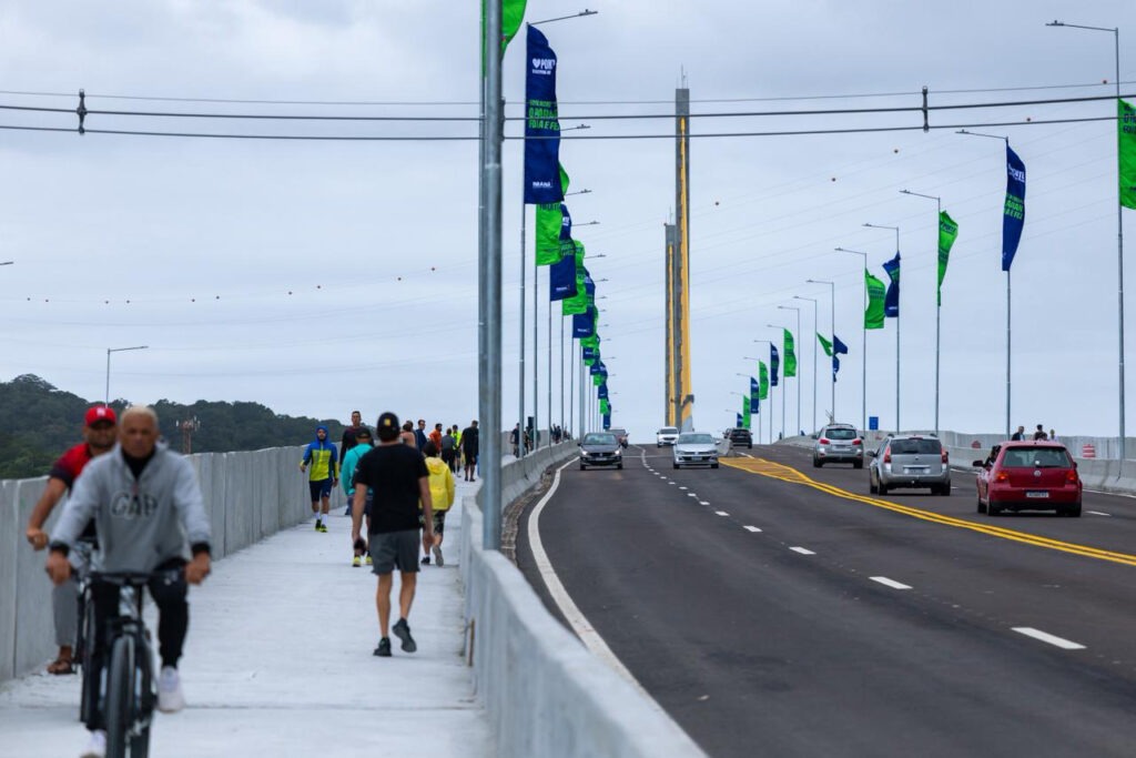 A Ponte de Guaratuba vista do ponto de vista do corredor de circulação de pedestres. Na imagem, é possível ver pessoas fazendo a travessia e carros circulando pela estrtutura
